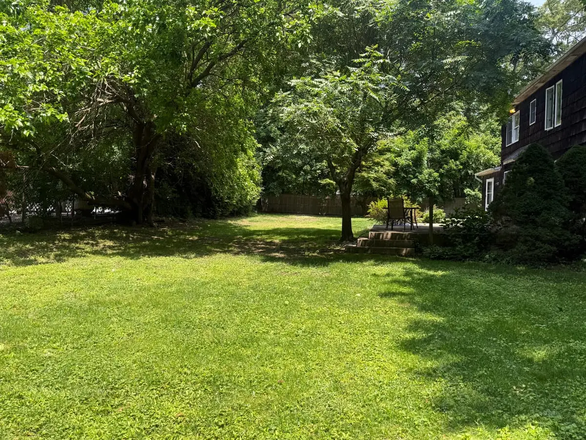 Selling a house for a job relocation in Smithtown: shaded backyard lawn beside a dark shingled colonial